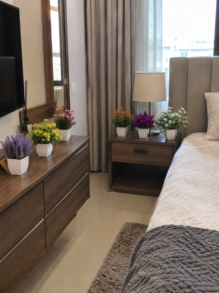  Small colorful artificial potted flowers arranged in groups on a wooden nightstand and dresser in a modern bedroom